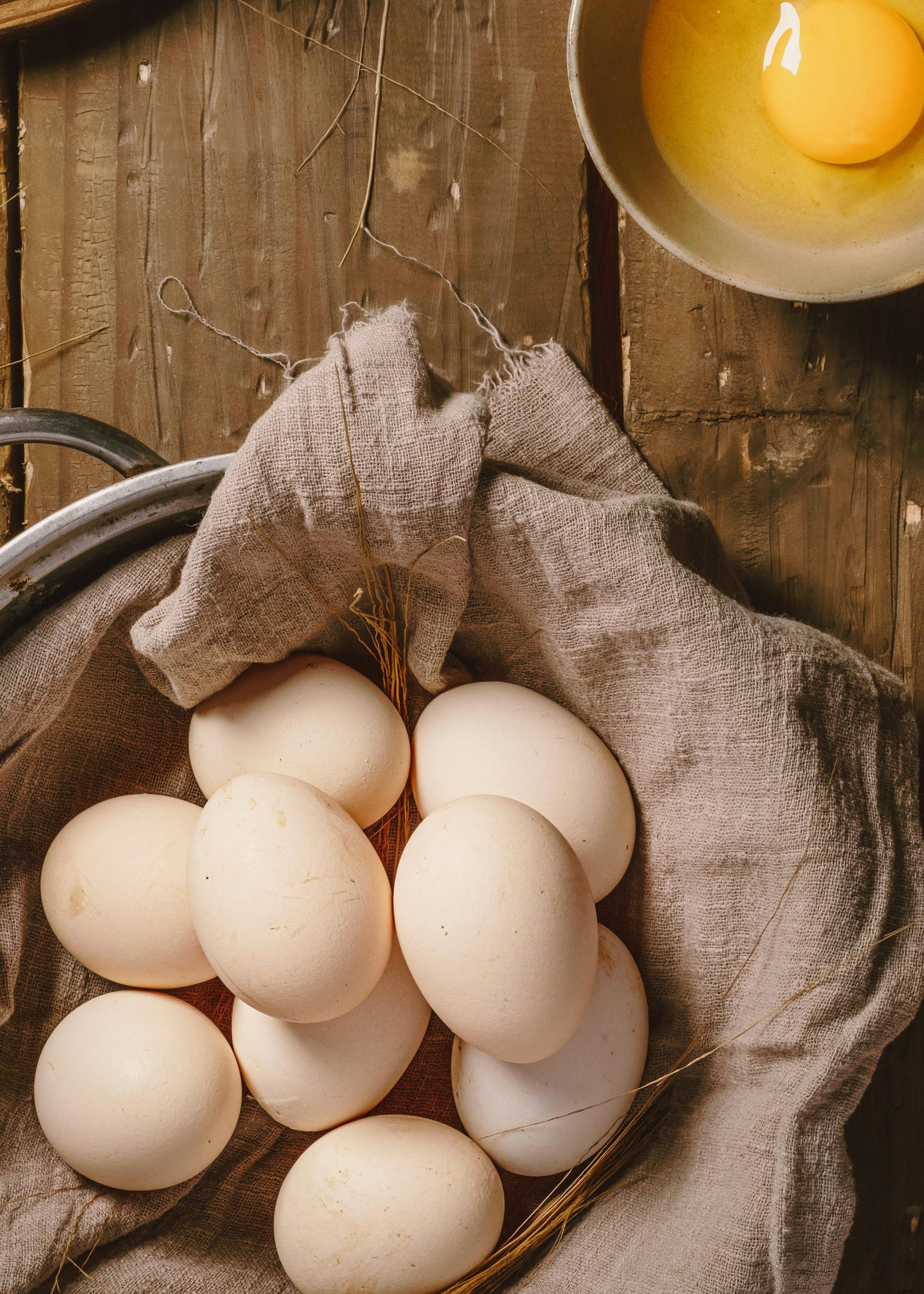 A rustic arrangement of farm-fresh eggs on cloth with a single cracked egg in a bowl.