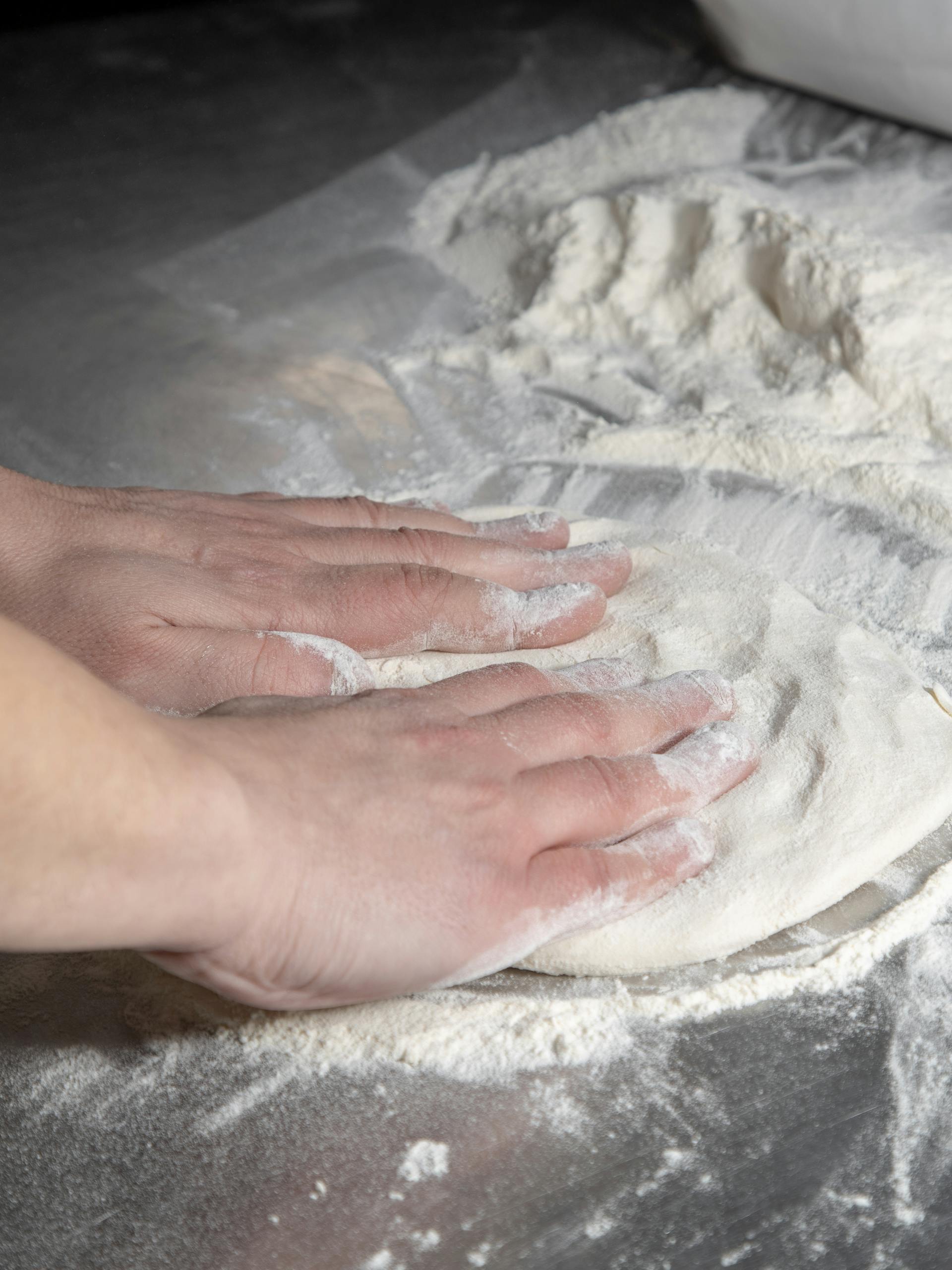 Close-up of hands kneading pizza dough on a floured surface, perfect for food preparation themes.