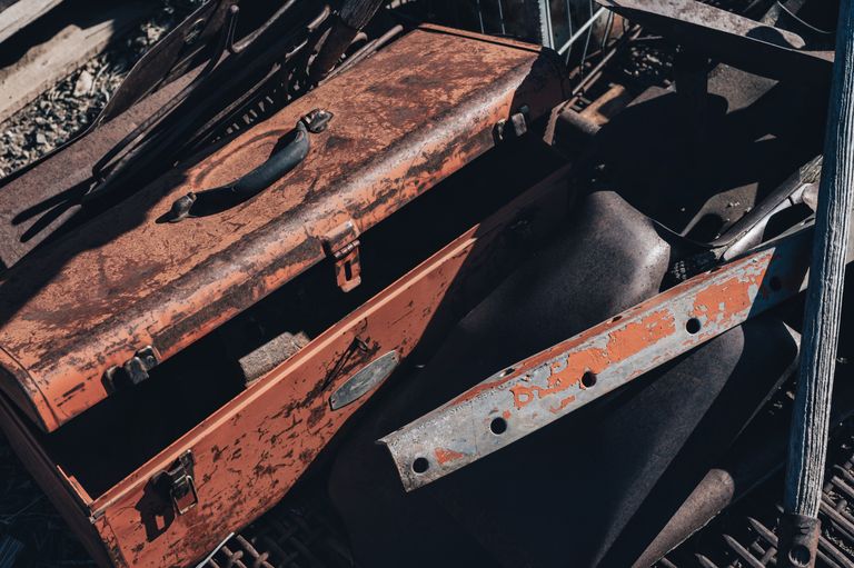 A vintage rusty toolbox amidst scrap metal pieces in a junkyard under sunlight.