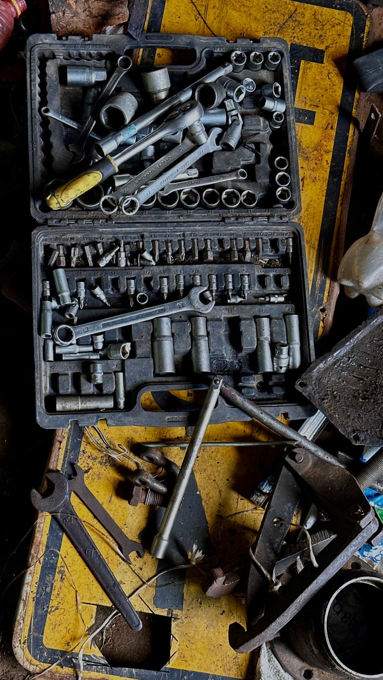 Overhead view of an old toolbox with assorted wrenches and sockets on a workbench.