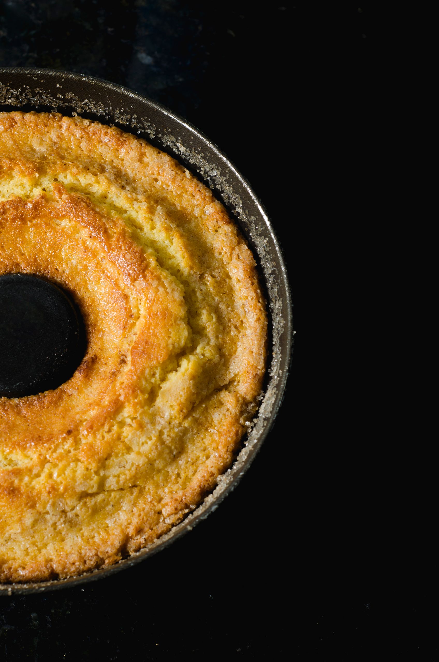 Close-up of a delicious homemade bundt cake with a golden crust against a dark background.