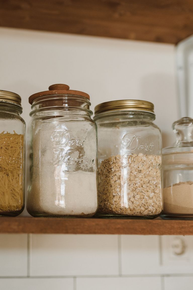 Close-up of glass jars filled with pasta, flour, and oatmeal on a wooden shelf, indoors.